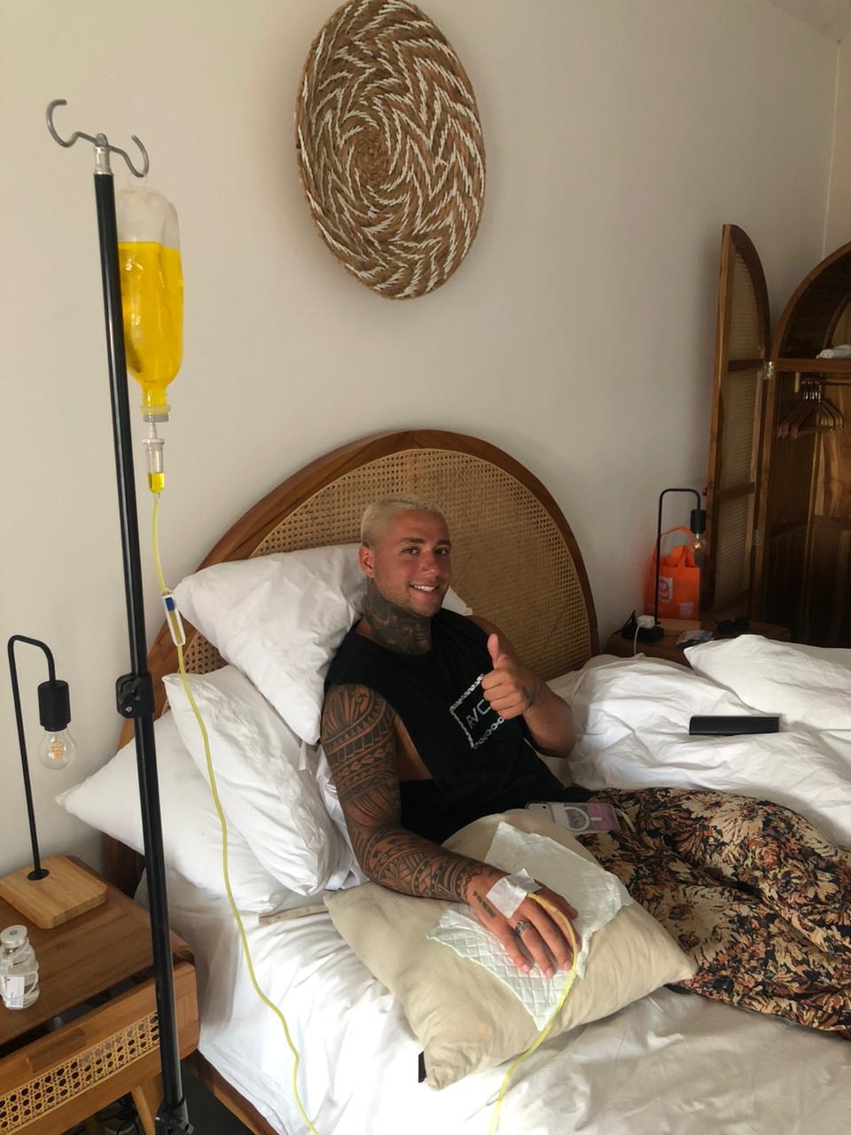 Active traveler with tattoos giving thumbs up while receiving IV drip therapy at Bali villa - Ever Well Health recovery