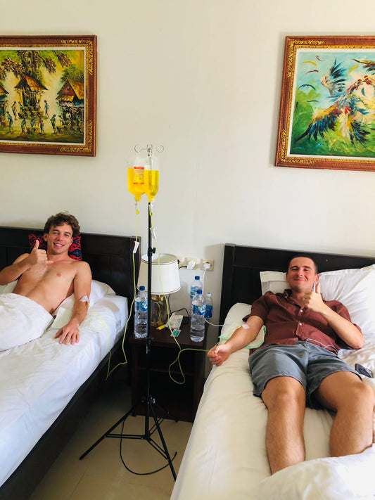 Two male friends giving thumbs up during group IV drip session at Bali hotel - Ever Well Health